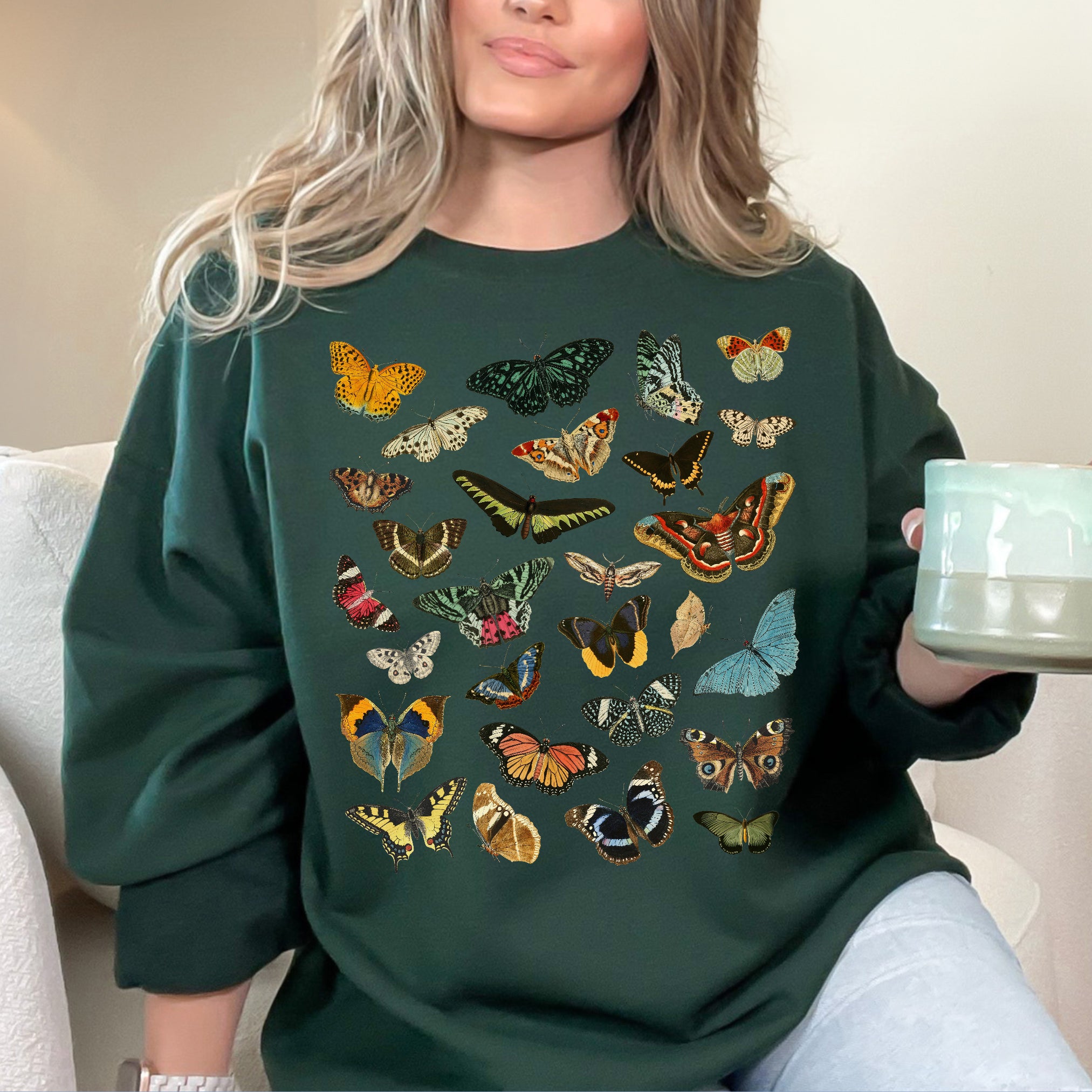 Person wearing a forest green sweatshirt with butterfly designs, holding a light blue mug.