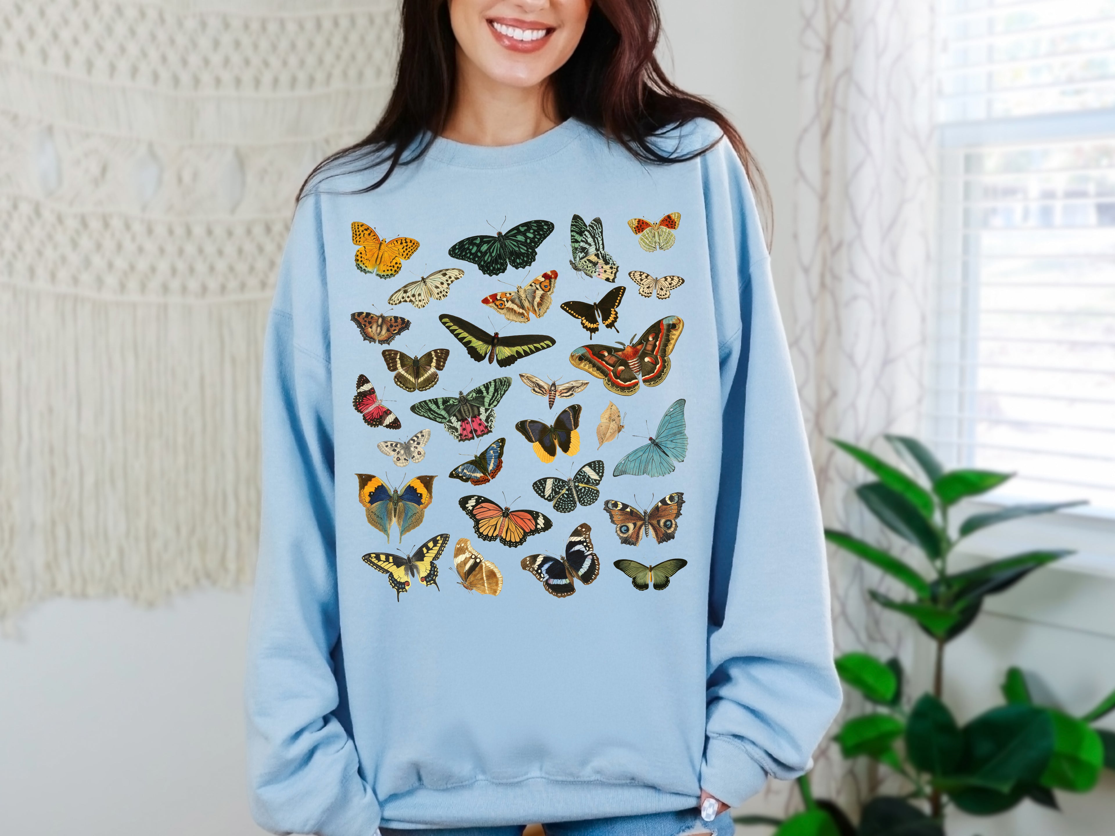 Person wearing a light blue Gildan sweatshirt with colorful butterfly & moth patterns in a home setting.