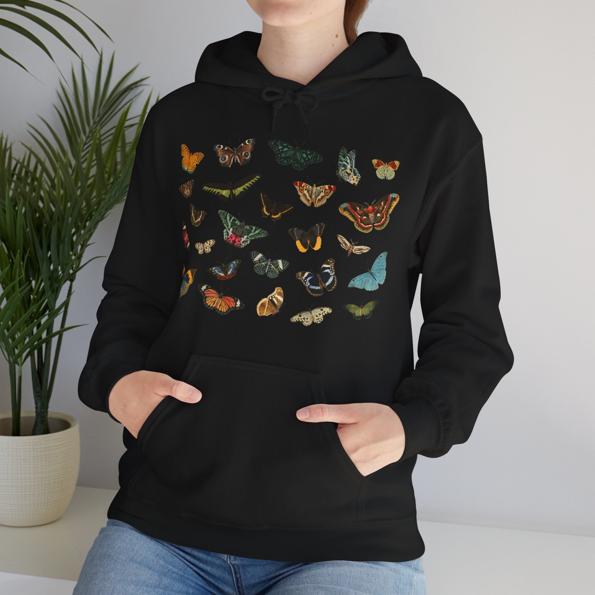 Person wearing a black Gildan hoodie with colorful butterfly & moth designs against a neutral background