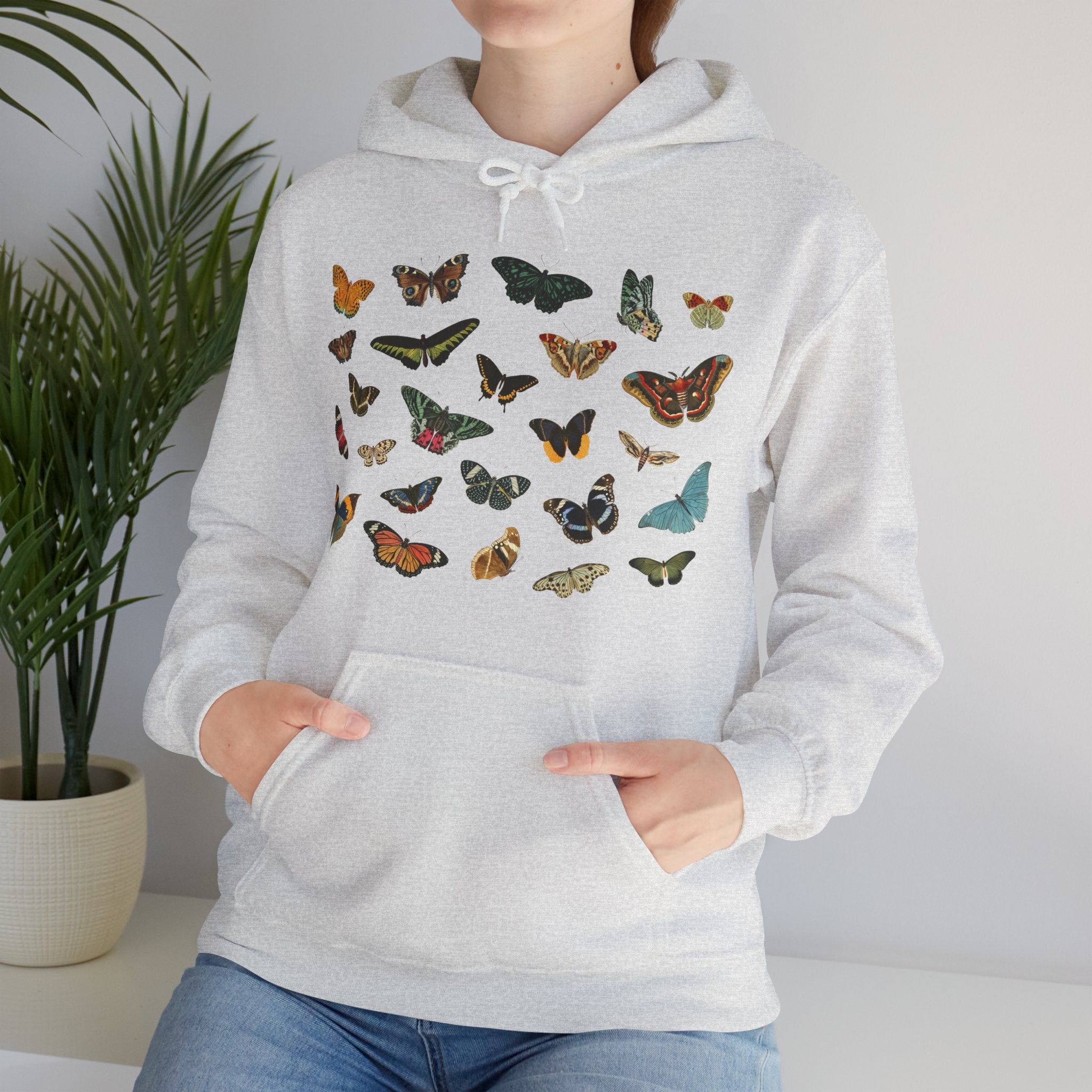 Person wearing a light gray ash hoodie with colorful butterfly designs against a neutral background, Gildan 18500