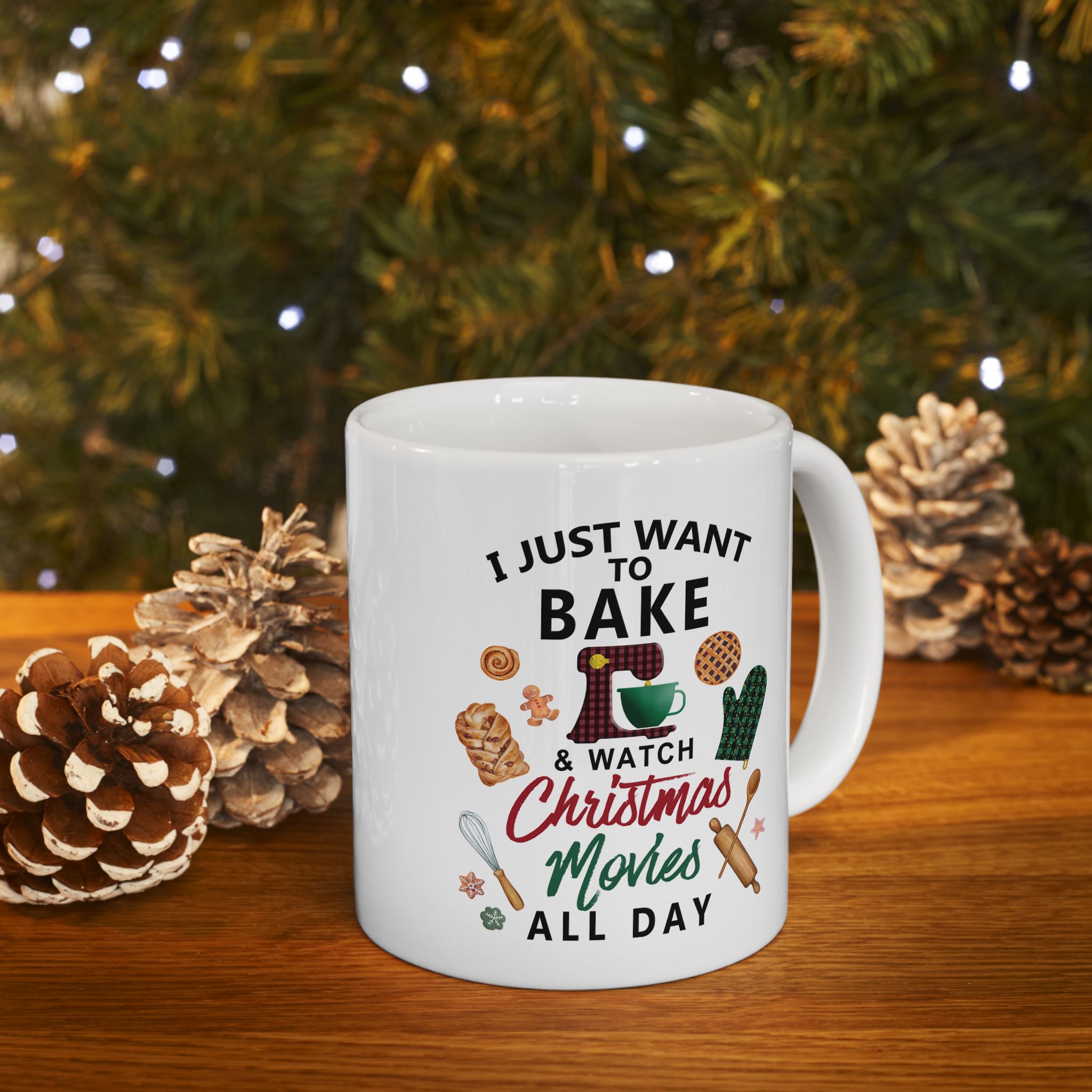 White mug with Christmas-themed text and graphics on a wooden surface with pinecones and a tree in the background.